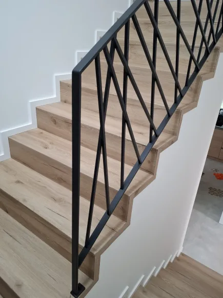 Detail černého zábradlí s diagonálním vzorem na schodech